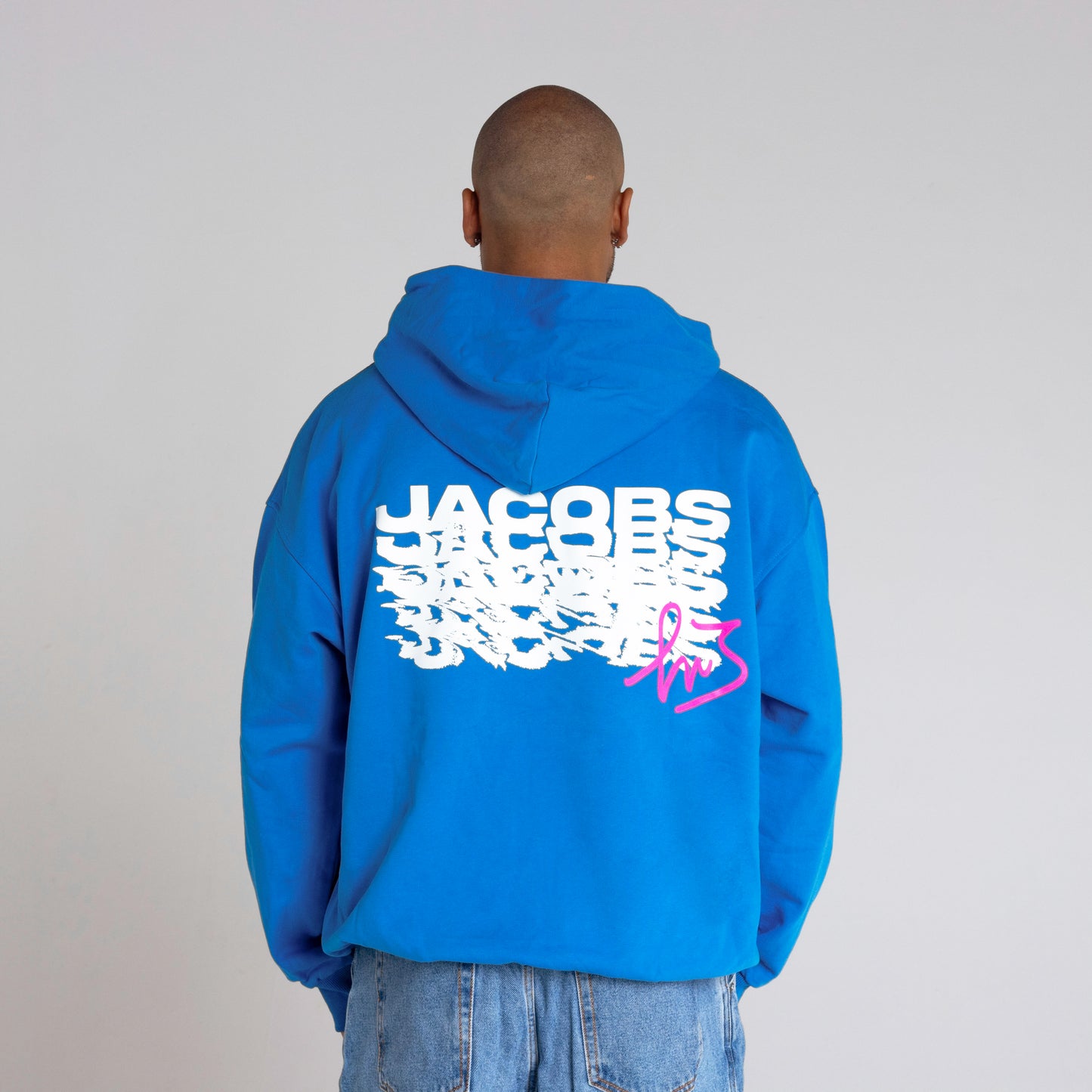 Logo distintivo sulla parte anteriore della felpa blu" "Schema ripetuto della scritta 'Jacobs' sulla parte posteriore della felpa blu in colore magenta con firma di Marcell Jacobs"