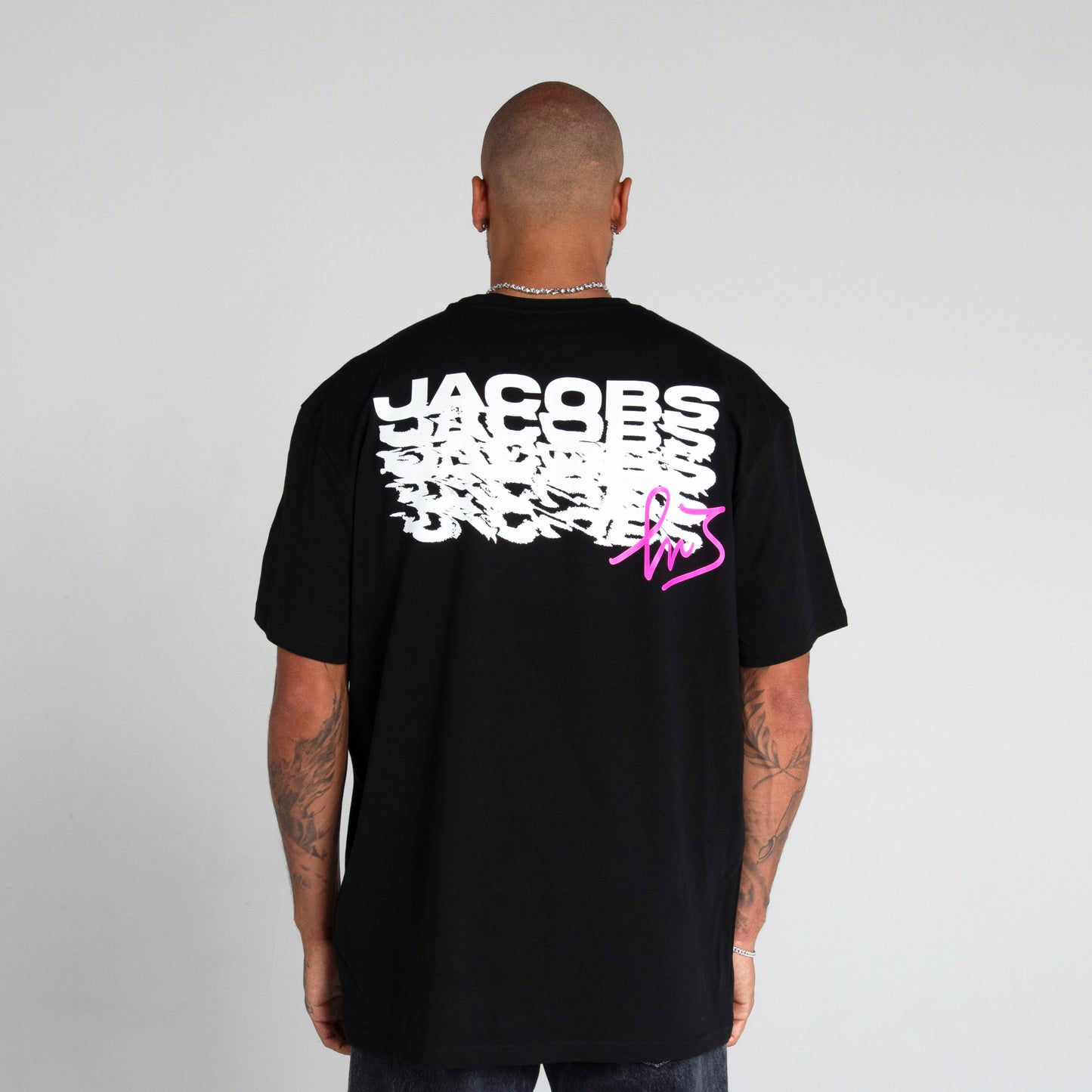 Logo distintivo sulla parte anteriore della maglia nera" "Schema ripetuto della scritta 'Jacobs' sulla parte posteriore della maglia nera in colore magenta con firma di Marcell Jacobs"